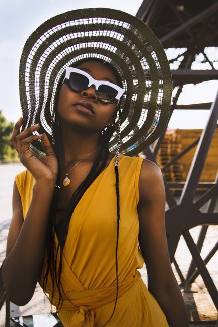 Fashionable black woman posing outdoors in a yellow dress and sunglasses.