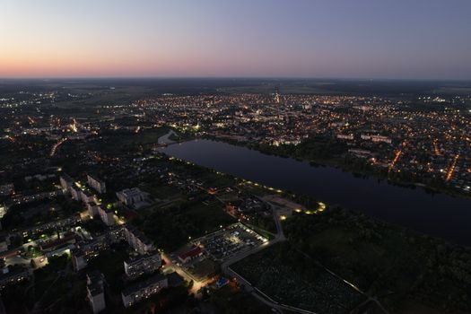 A stunning aerial shot of Kovel, Ukraine, showcasing city lights and a serene body of water at dusk.