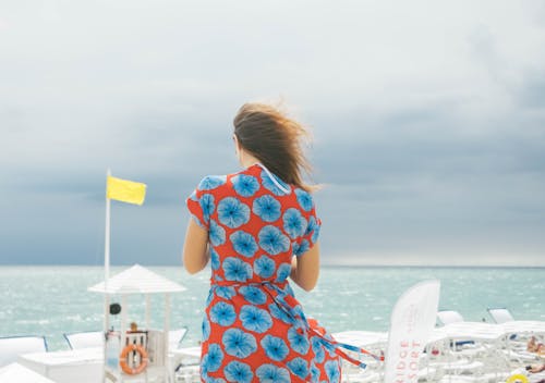 Woman in Red and Blue Floral Dress Standing Near Body of Water