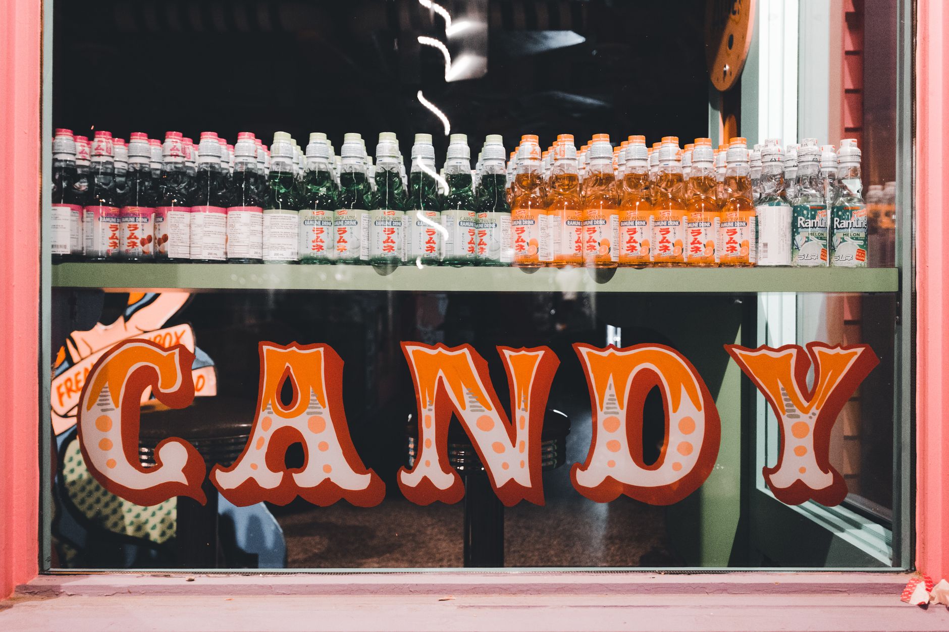 An array of colorful beverage bottles showcased in a vintage-style candy shop window.