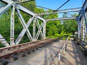 Old metal railway bridge surrounded by lush green trees in Tarsac, Occitanie, France.