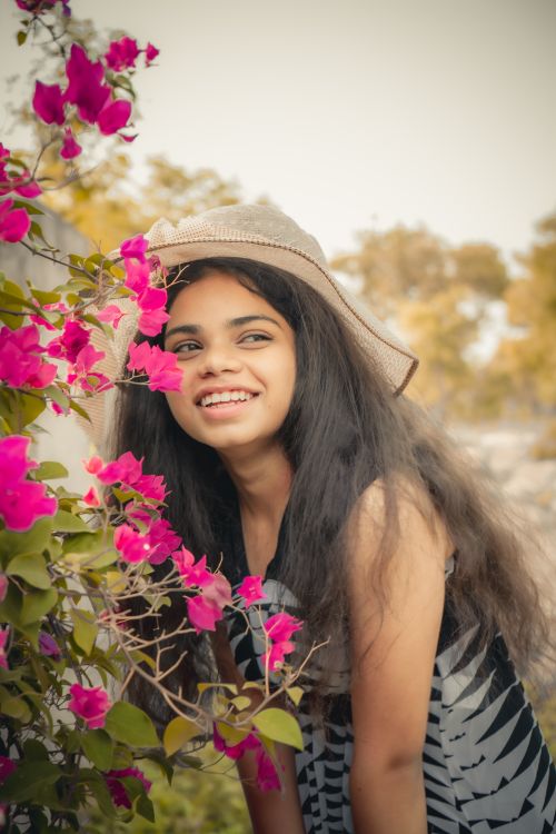 Free Young woman in sun hat enjoying pink bougainvillea blooms outdoors, radiating joy. Stock Photo