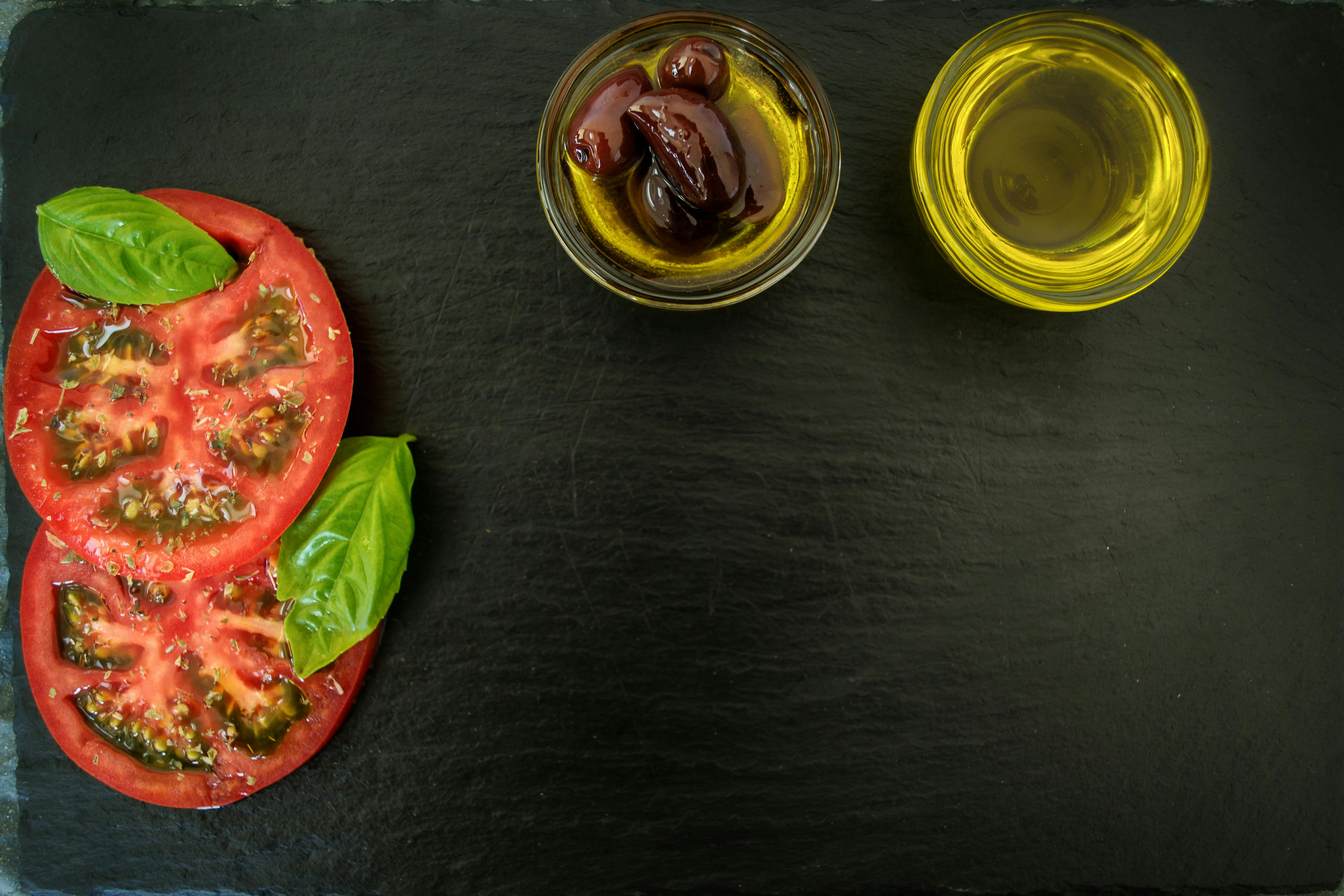Sliced Tomatoes With Basil Leaves and Two Cooking Oils on Black Wooden