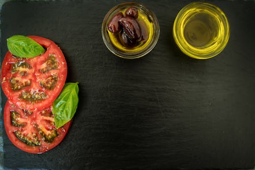 Free Sliced Tomatoes With Basil Leaves and Two Cooking Oils on Black Wooden Surface Stock Photo