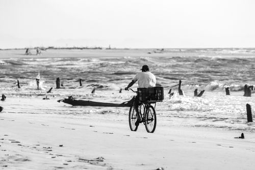 Free A lone cyclist enjoys a scenic ride along a Brazilian beach with waves in the background. Stock Photo