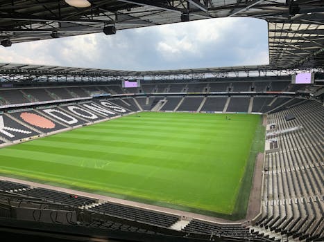 Empty soccer stadium with lush green field and seating, captured during the day.