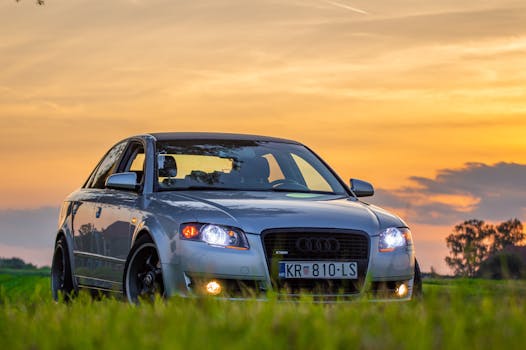 Elegant silver car parked in a field with a stunning sunset background, showcasing luxury and tranquility.