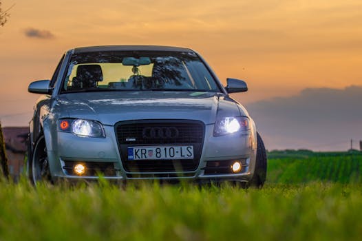 Luxurious car parked in green field during sunset with headlights on.