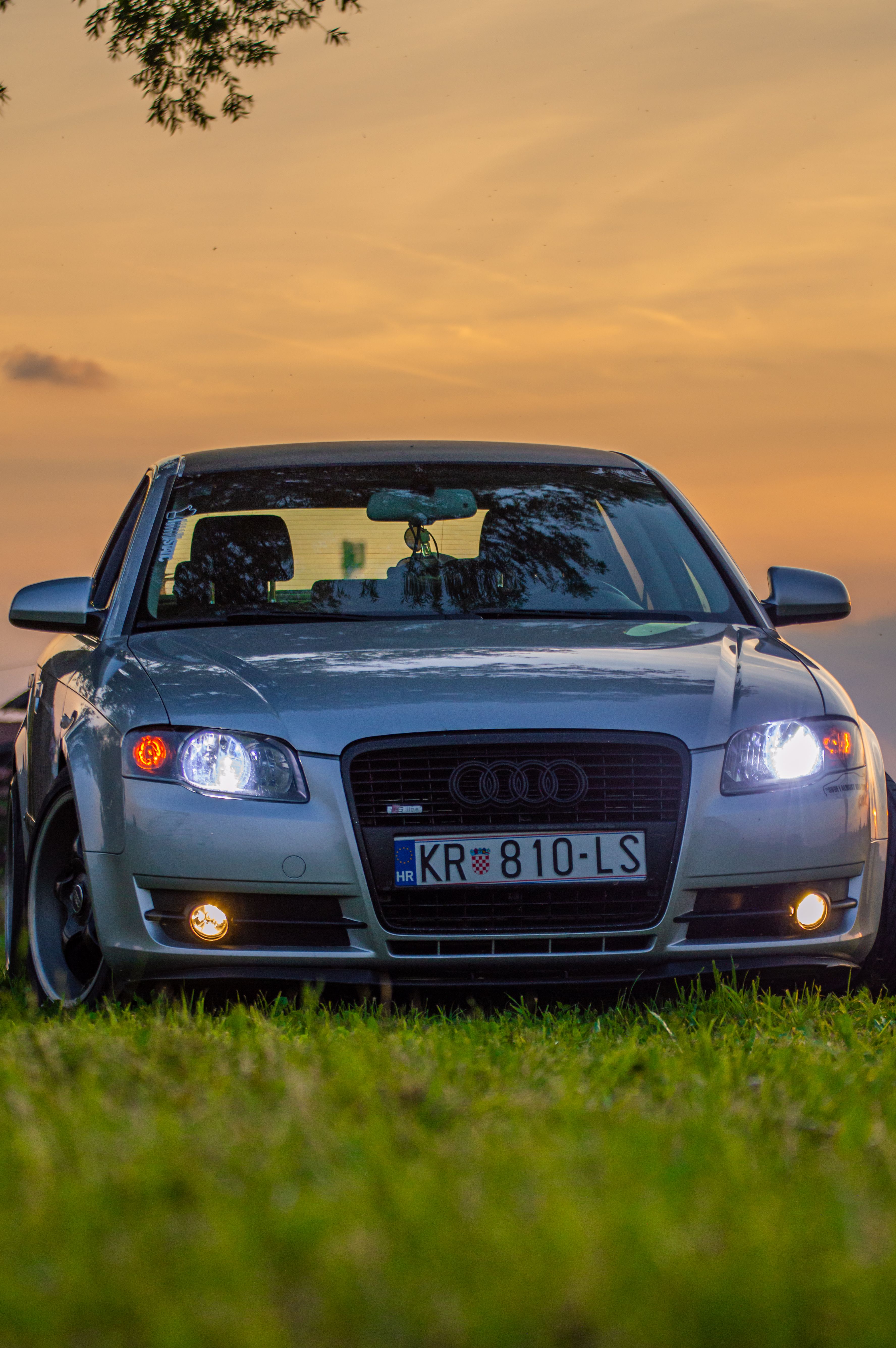 Front view of a luxurious Audi car parked in a grassy field at sunset.