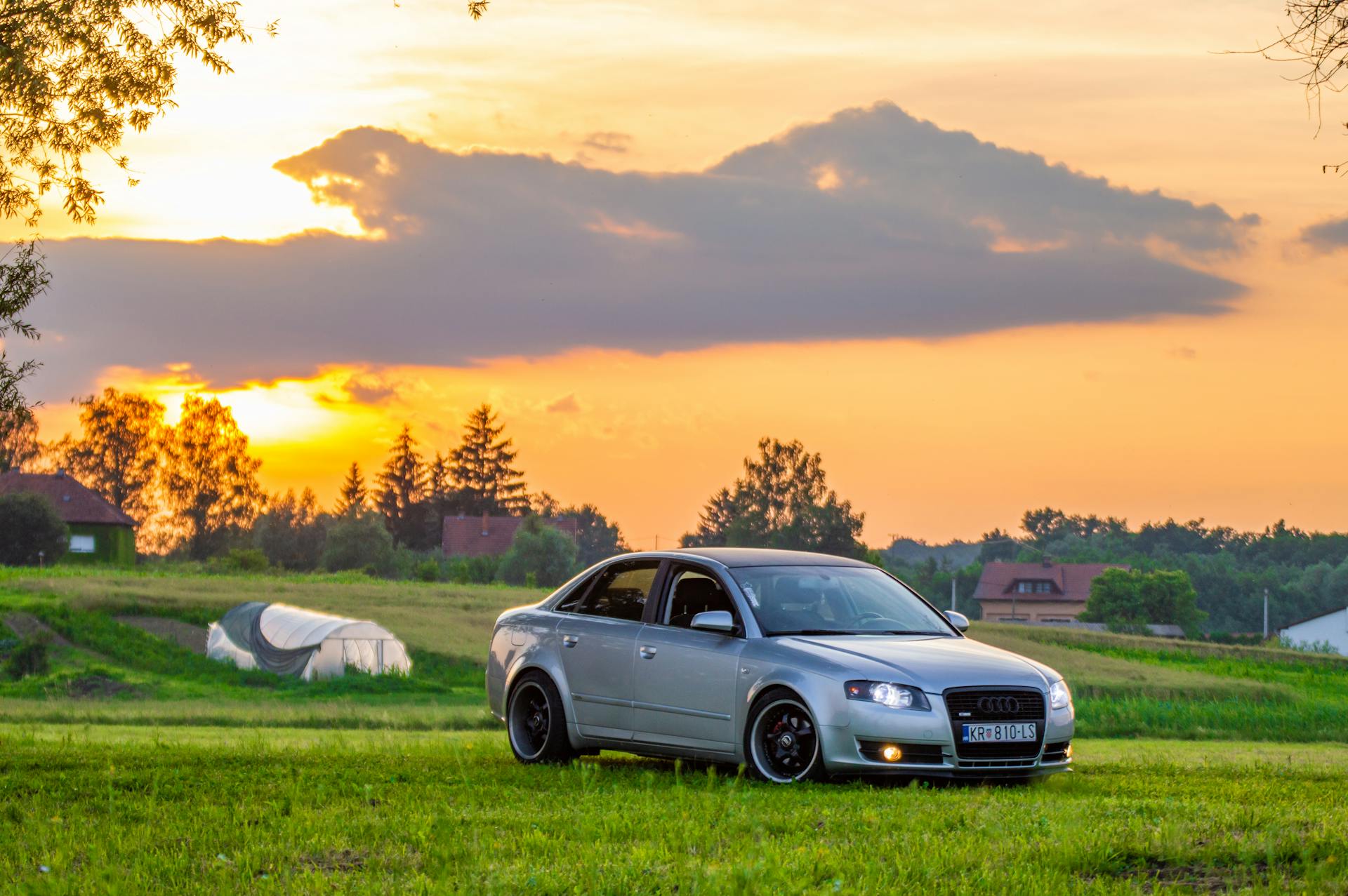 A luxurious Audi car parked on a grassy field during a stunning sunset, exuding elegance and sophistication.