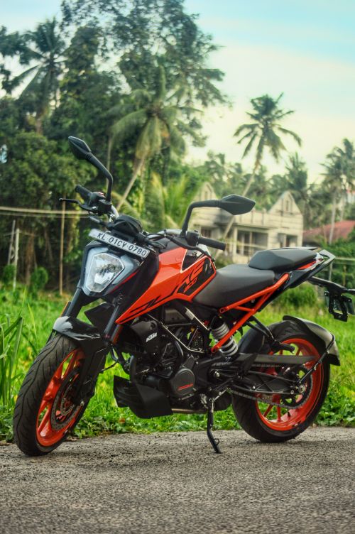 Free Vibrant orange motorcycle parked on concrete with lush green tropical backdrop in India. Stock Photo