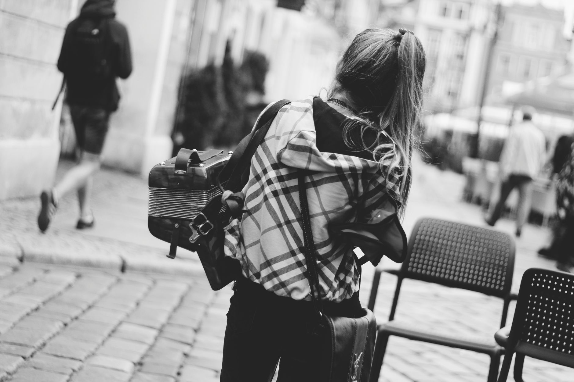Monochrome image of a woman with an accordion walking in a bustling city street.