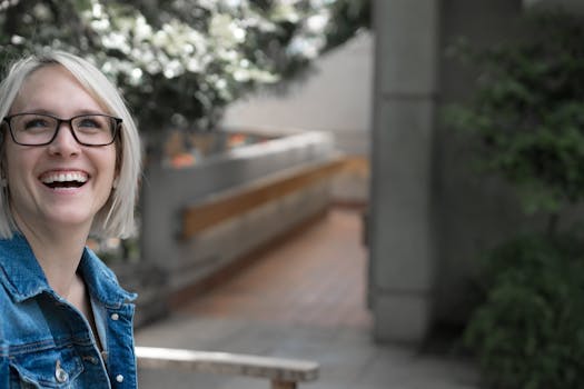 一个戴着眼镜、穿着牛仔夹克的女人在宁静的户外环境中快乐地微笑