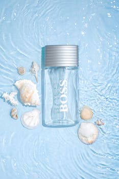 A product shot of a clear perfume bottle surrounded by seashells on a rippled water background.