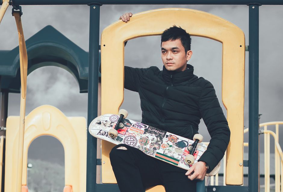 Confident young man in jacket posing with skateboard in a colorful playground setting.