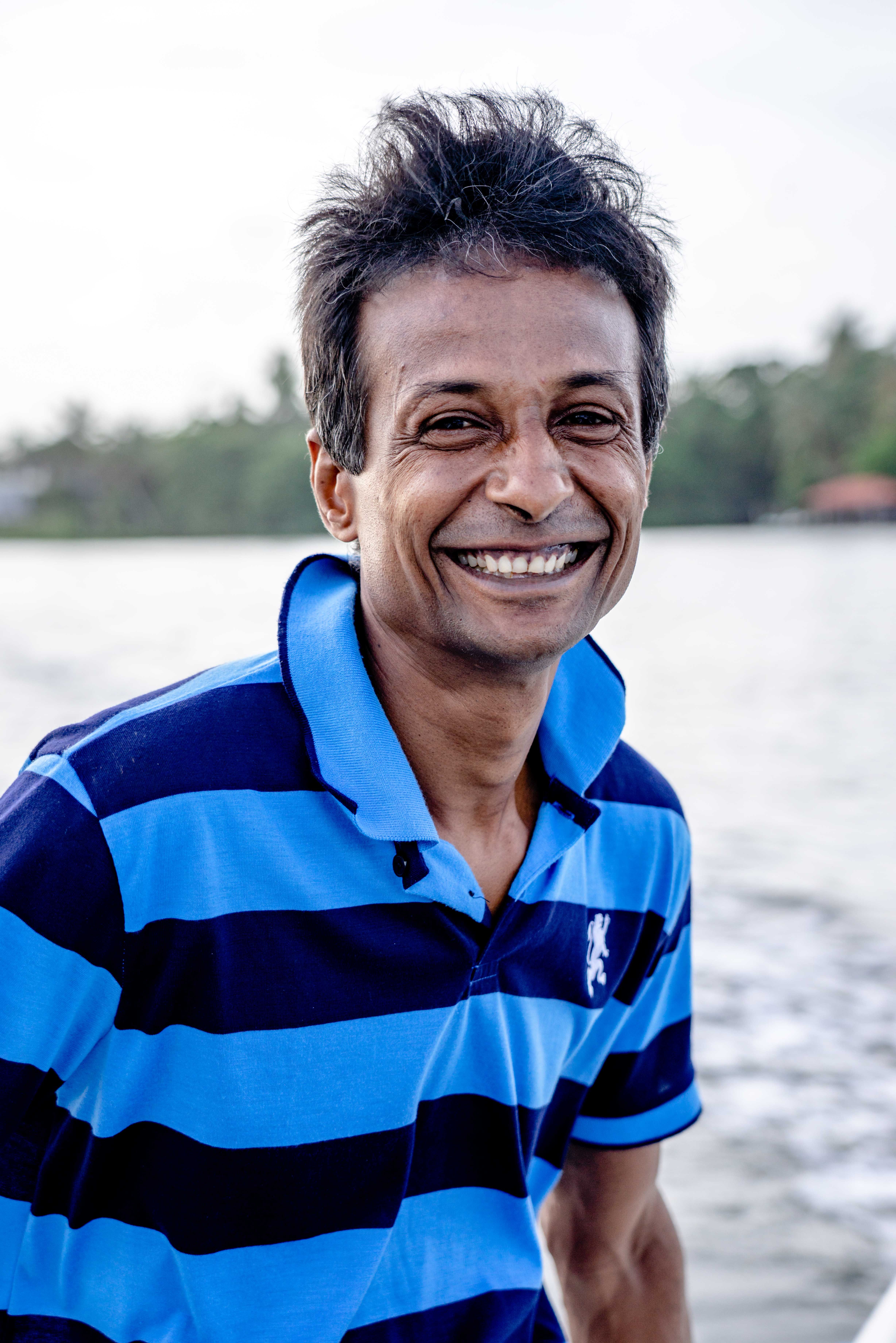 Joyful portrait of a senior man with a warm smile wearing a blue striped polo shirt by the seaside.