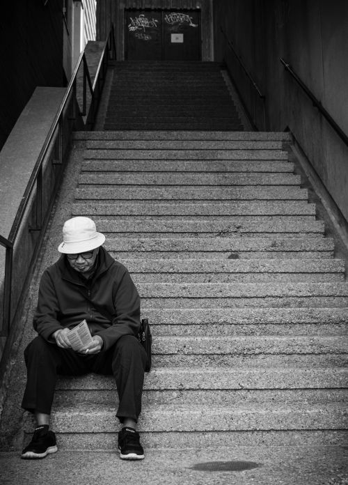 Free Black and white image of an elderly man sitting and reading on a concrete staircase. Stock Photo