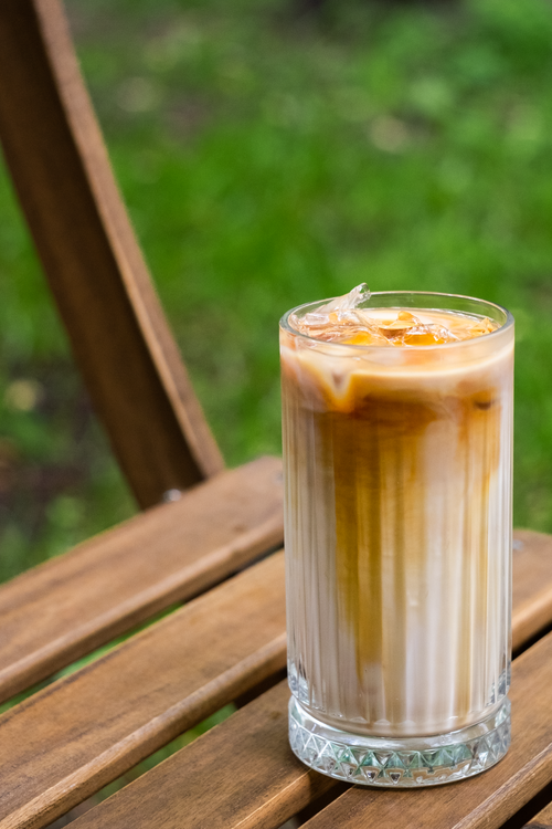 Free Refreshing iced coffee in a tall glass set on a wooden chair in a garden. Stock Photo