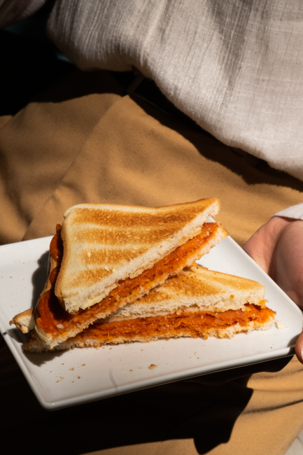 A pimento cheese sandwich cut diagonally on a plate, showing the flecked orange-and-red spread between two slices of soft white bread.