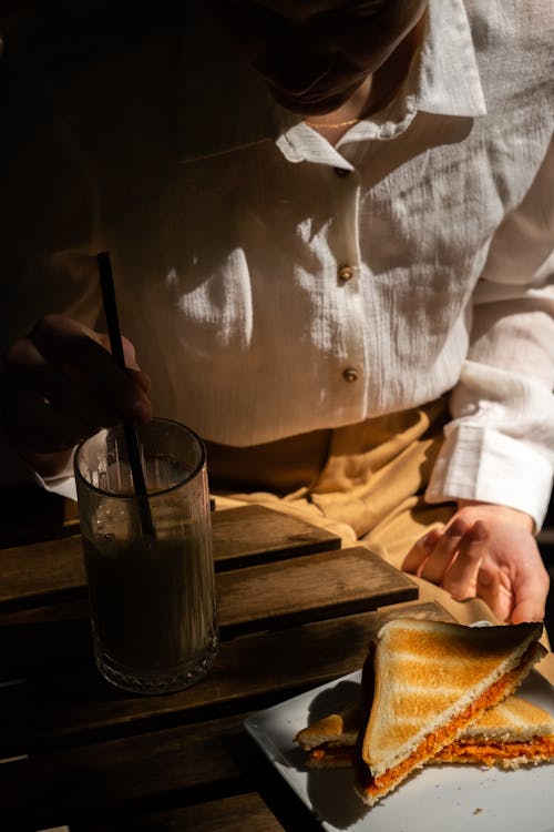 A Person in White Long Sleeves Sitting Near the Wooden Table with Food