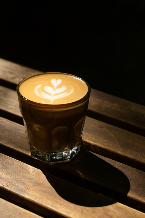 Free A beautifully crafted espresso with latte art sits on a sunlit wooden table. Stock Photo
