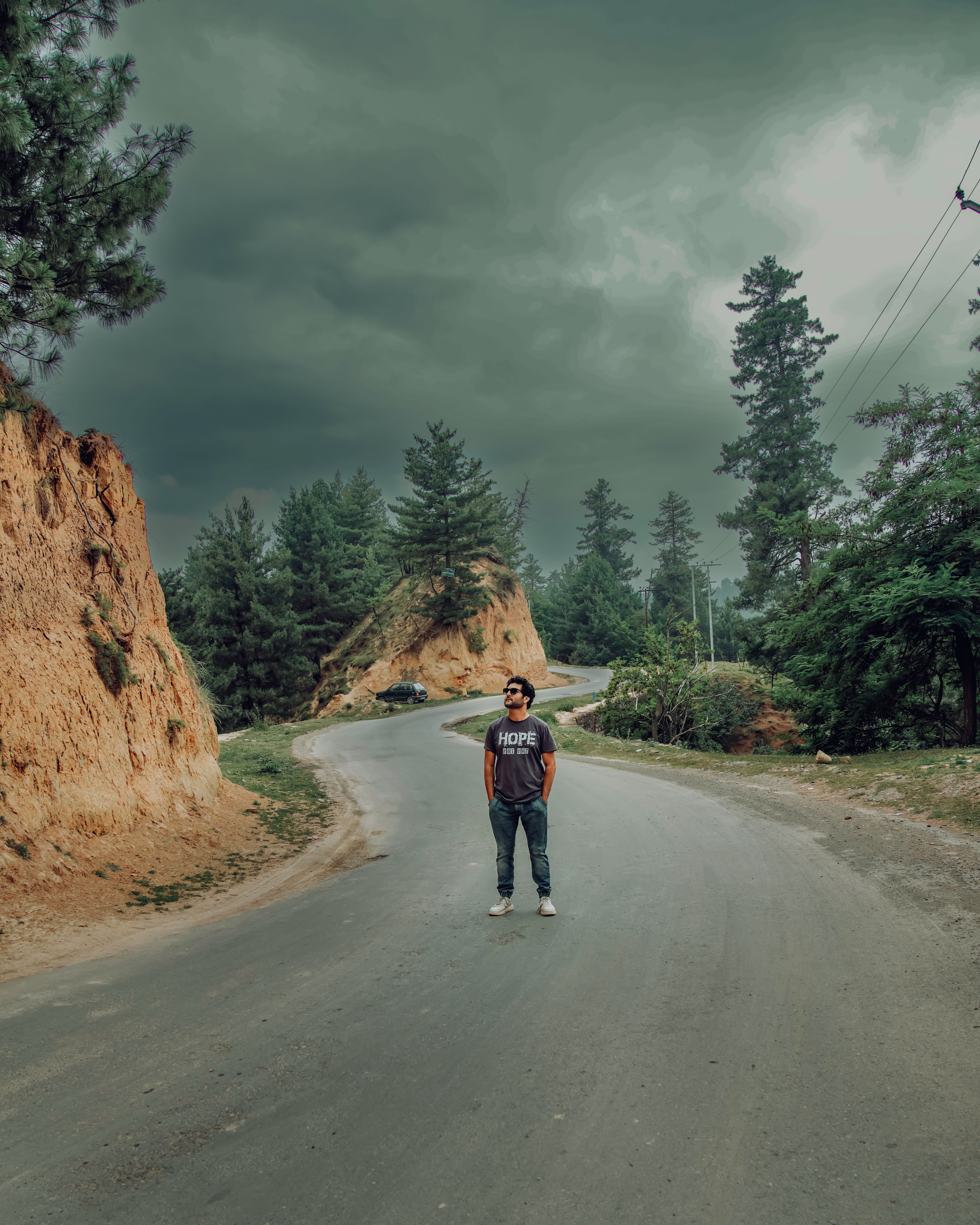 Man standing on a winding road in scenic Yousmarg with cloudy sky.