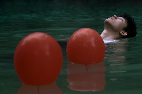 Man Floating in the Lake Besides Red Balloons