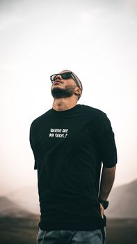 A bearded man in a black shirt with sunglasses, looking up outdoors in Iran.