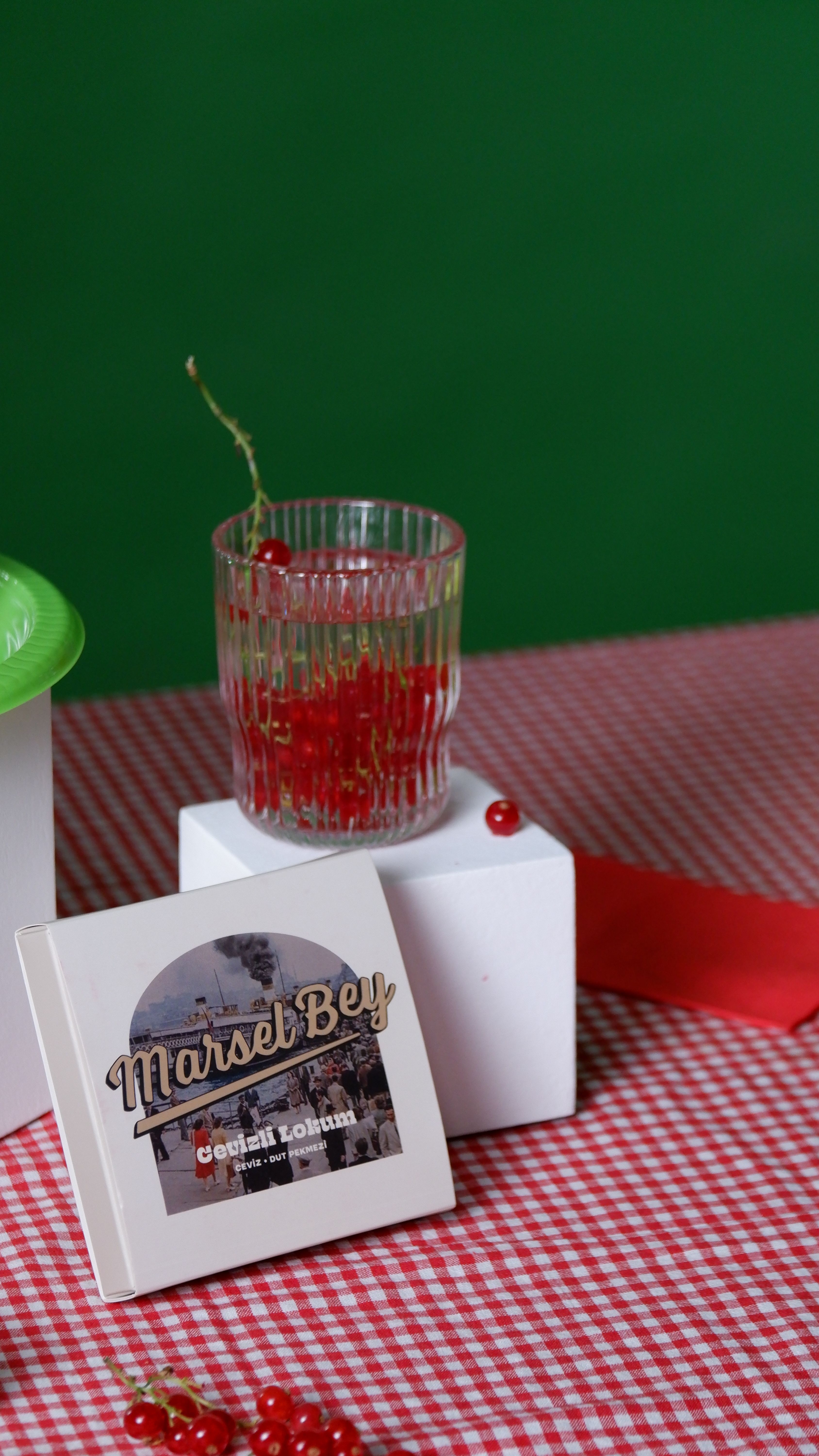 A glass filled with red berries on a checkered tablecloth with a green backdrop, perfect for culinary presentations.