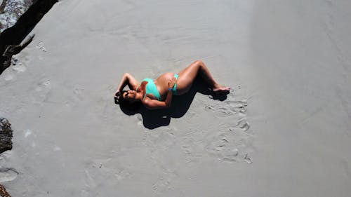 Free A Pregnant Woman Lying on Beach Sand Stock Photo