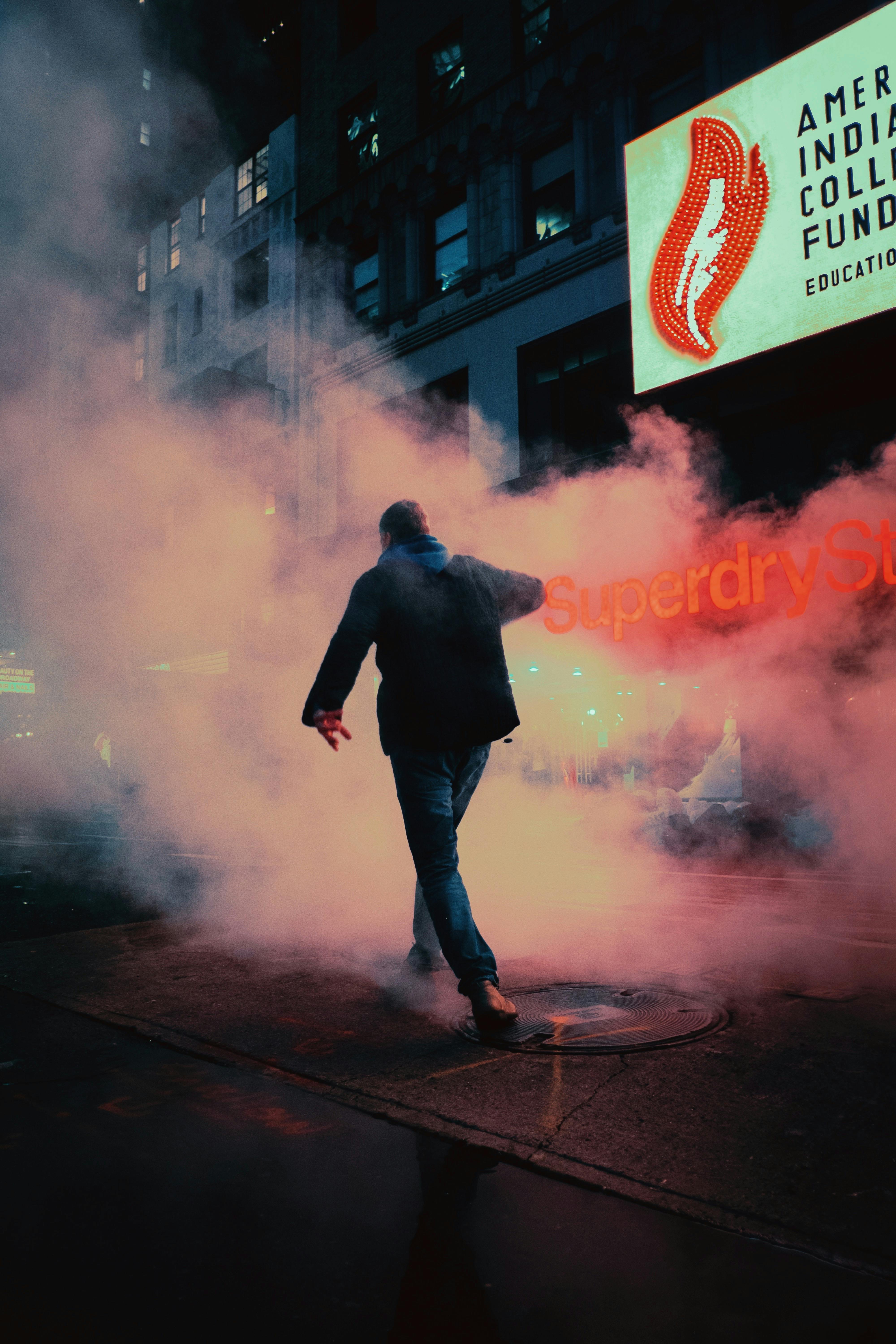 A lone figure walks through neon-lit streets amidst swirling mist, evoking a sense of mystery and fantasy.