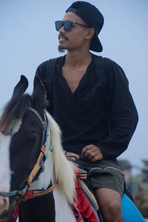 Man in Black Long Sleeves Riding a White and Black Horse