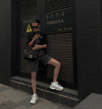Fashionable woman in sunglasses with handbag in Kyiv, showcasing urban street style.
