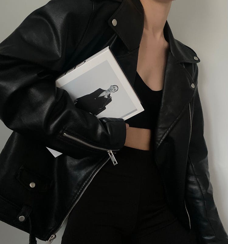 A Person In A Black Leather Jacket Holding A Book