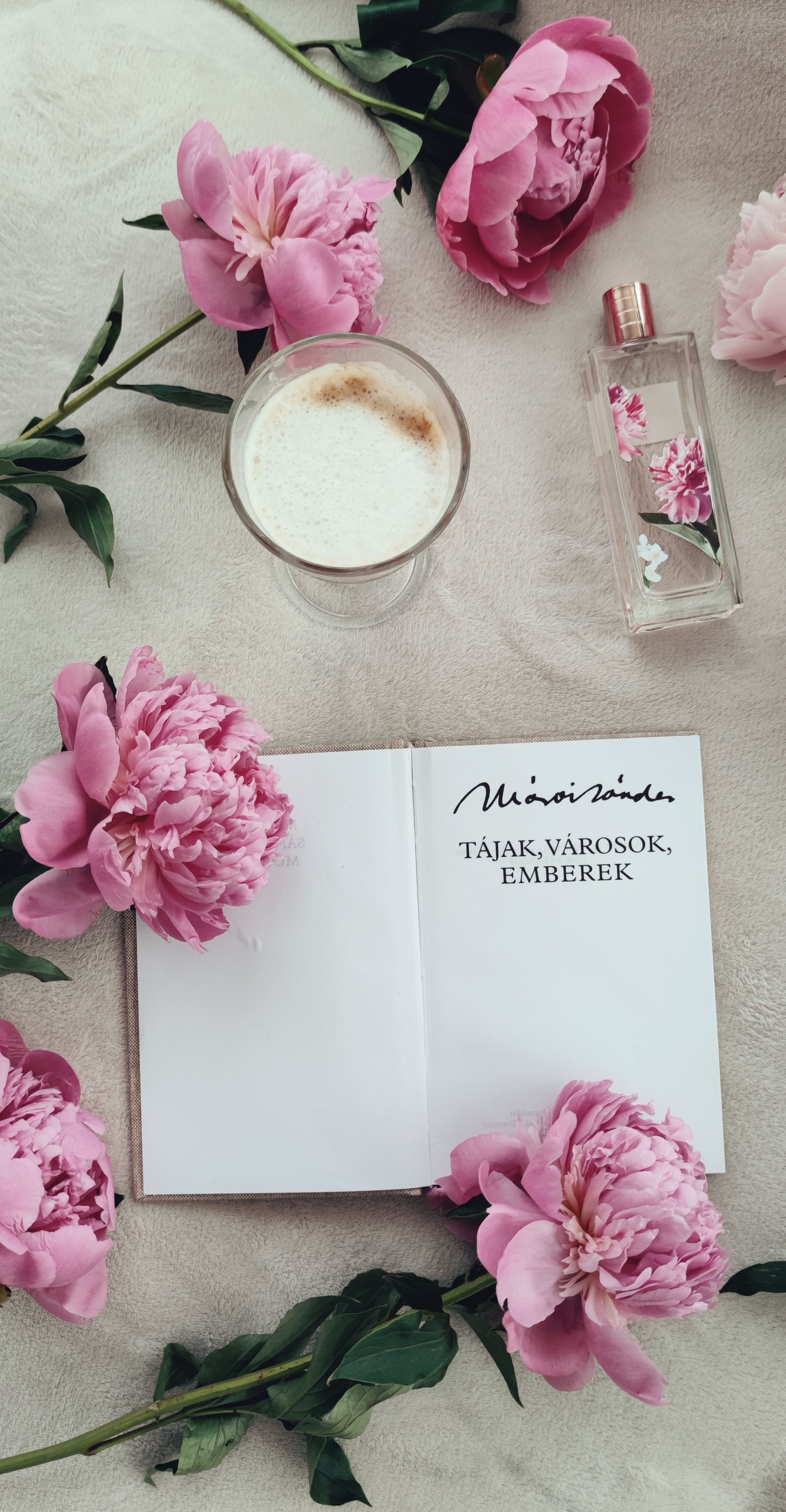 Artistic flat lay of an open book, pink peonies, and a coffee cup in a tranquil setting.