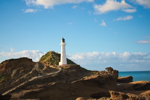 Free Scenic view of Castlepoint Lighthouse on a rocky cliff edge against a bright blue sky. Stock Photo