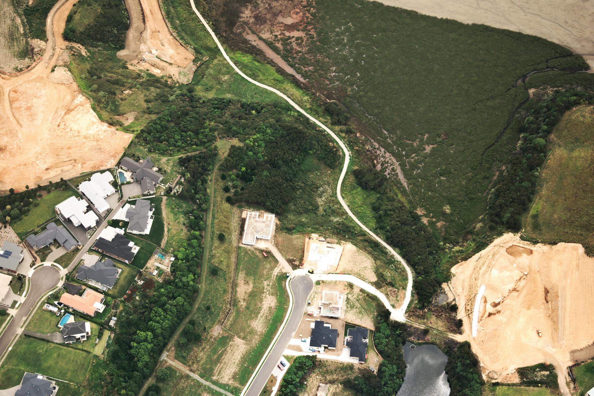 Aerial shot of a suburban housing development with roads, green spaces, and construction sites.