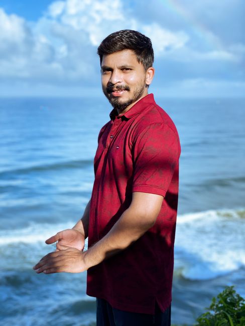 Happy man standing by the ocean in a red polo shirt, enjoying a sunny day by the sea.