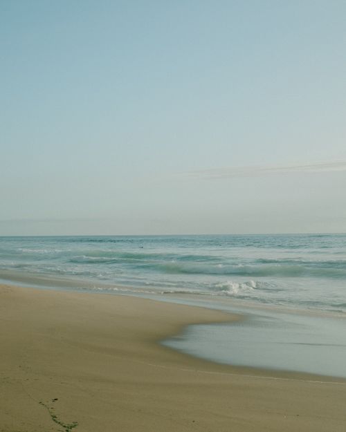 Free Calm waves gently reaching a quiet beach under a clear sky, perfect for relaxation and solitude. Stock Photo