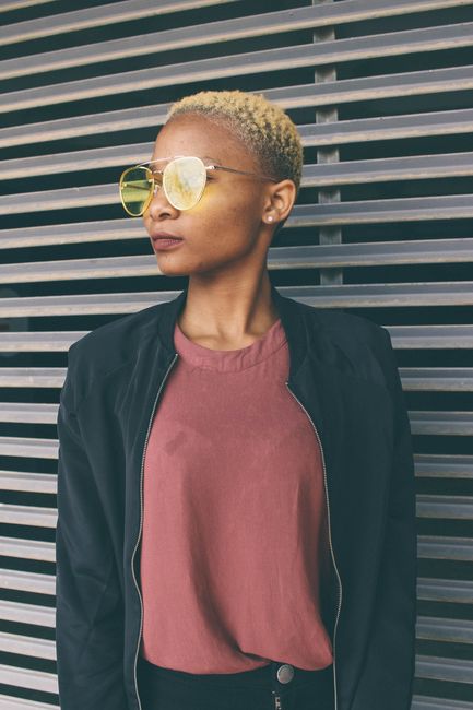 Portrait of a fashionable woman wearing sunglasses and a jacket, set against a modern urban backdrop.