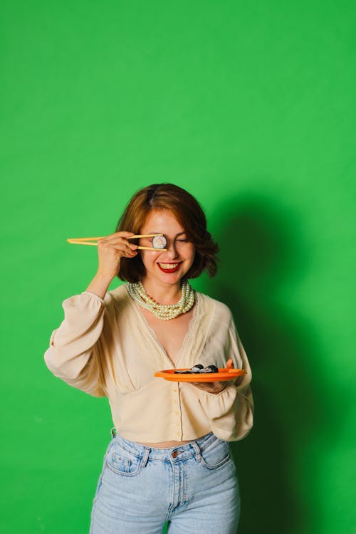 Woman Holding Suchi on Chop Sticks Against Green Background 