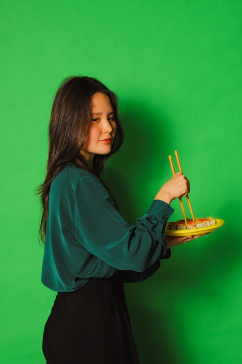 A Woman in Blue Long Sleeves Holding a Plate and Chopsticks