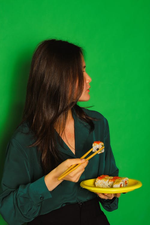 A Woman in Blue Long Sleeves Holding a Chopsticks with Sushi