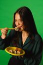 Studio Shot of a Brunette Eating Sushi on Green Background