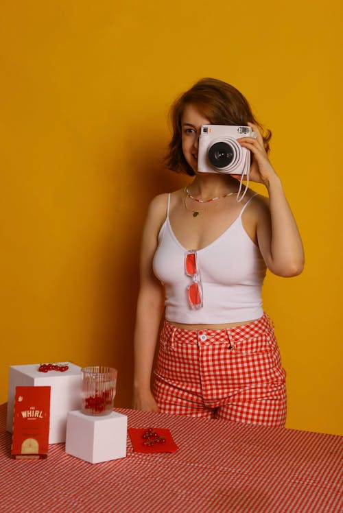 Woman in White Tank Top and Checkered Pants Holding White Camera 