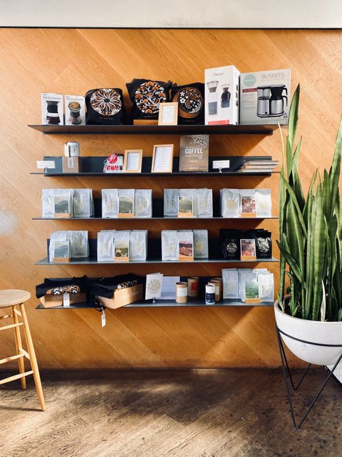 Free Neatly organized coffee shop shelves featuring products, decor, and a potted plant against a wooden backdrop. Stock Photo