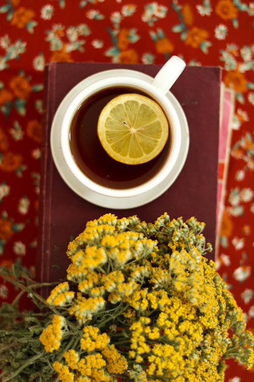 Cup of Tea on a Pile of Books Near Yellow Flowers