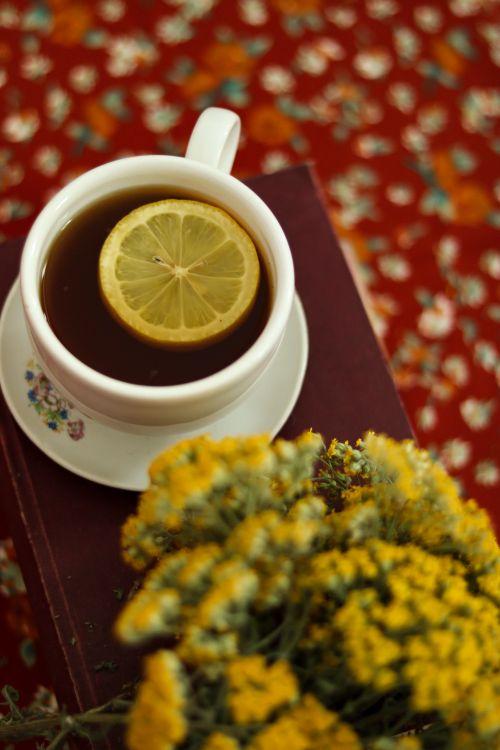 Free A cozy scene featuring a cup of tea with a lemon slice, styled with yellow flowers on a floral background. Stock Photo