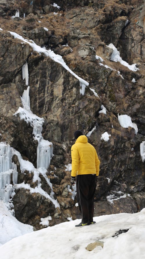 Person in Yellow Bubble Jacket standing near a Rock Formation 