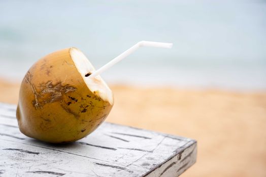 Close-up of a coconut with a straw on a wooden table by the beach.